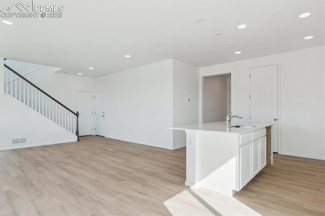 empty room with visible vents, light wood-style flooring, recessed lighting, a sink, and stairs