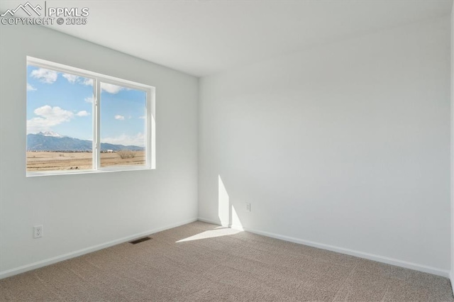 carpeted empty room featuring visible vents, baseboards, and a mountain view