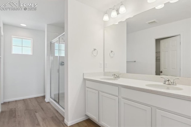 bathroom with visible vents, a shower stall, double vanity, wood finished floors, and a sink