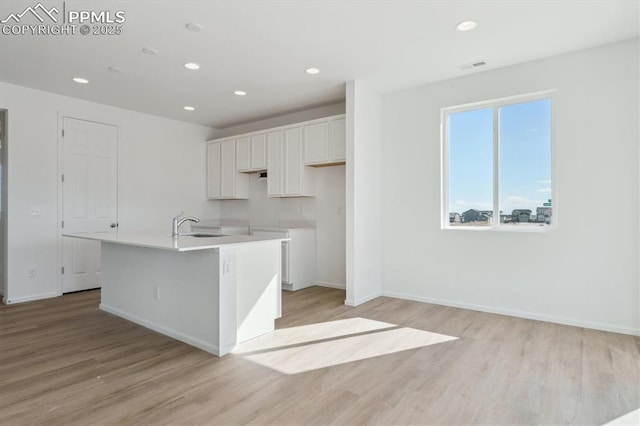 kitchen with light wood finished floors, recessed lighting, white cabinetry, and an island with sink