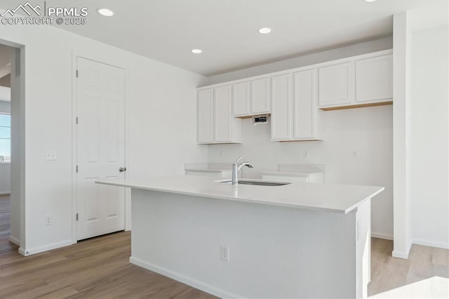 kitchen featuring a kitchen island with sink, white cabinetry, light wood-type flooring, and a sink