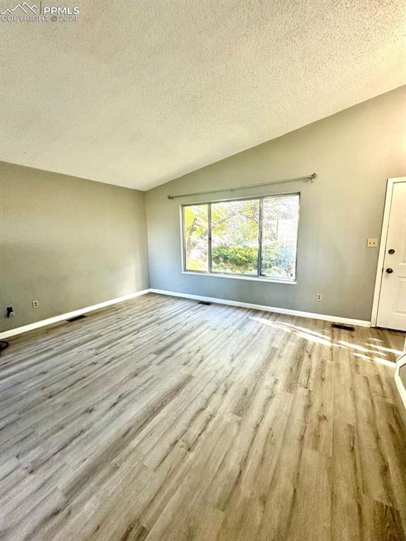 unfurnished room with light wood-type flooring, lofted ceiling, and a textured ceiling