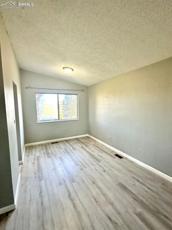 spare room with a textured ceiling, light hardwood / wood-style flooring, and vaulted ceiling