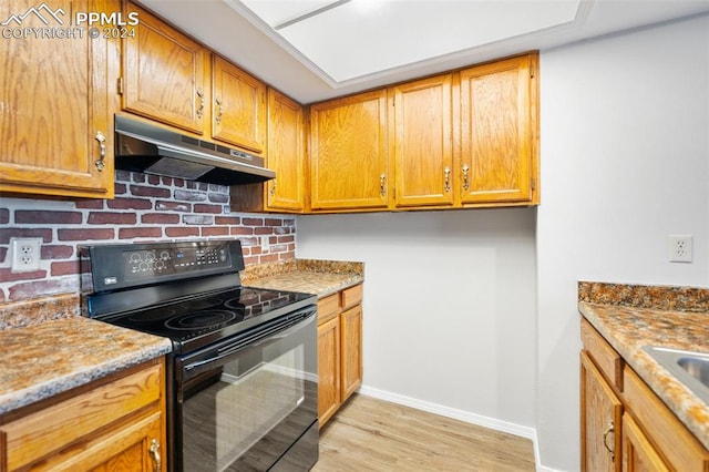 kitchen featuring black electric range oven, light hardwood / wood-style flooring, and light stone counters