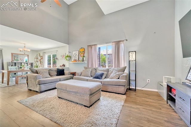 living room with a high ceiling, ceiling fan with notable chandelier, light hardwood / wood-style flooring, and plenty of natural light