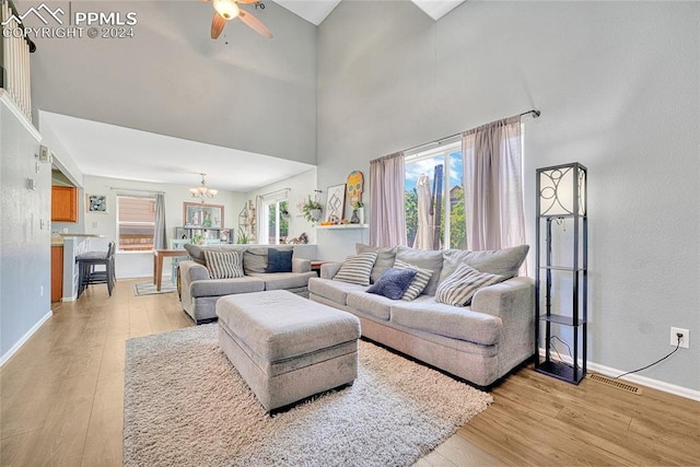 living room with a towering ceiling, ceiling fan with notable chandelier, and light hardwood / wood-style flooring