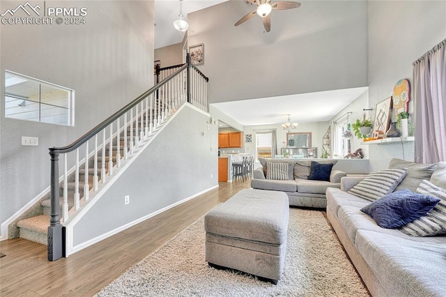 living room featuring ceiling fan with notable chandelier, a towering ceiling, and light hardwood / wood-style floors