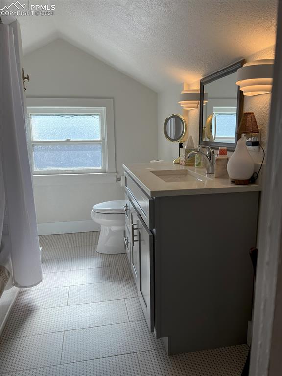 bathroom with tile patterned flooring, a textured ceiling, vaulted ceiling, toilet, and vanity