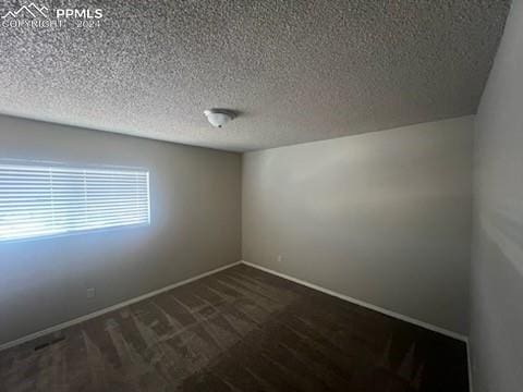 unfurnished room featuring dark carpet and a textured ceiling