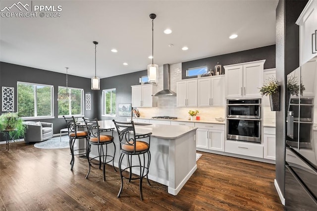 kitchen featuring white cabinets, a center island with sink, dark hardwood / wood-style floors, and wall chimney range hood