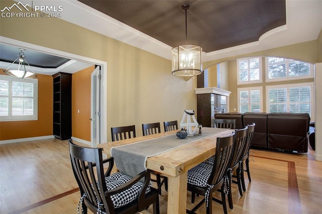 dining room featuring a notable chandelier, a raised ceiling, and light hardwood / wood-style flooring