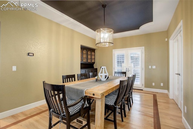 dining room with french doors, light wood-type flooring, a raised ceiling, and a notable chandelier