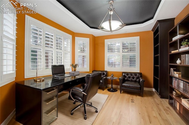 office area with light hardwood / wood-style floors and a raised ceiling