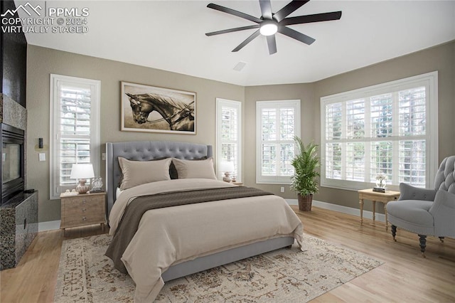 bedroom with ceiling fan, a high end fireplace, and light wood-type flooring