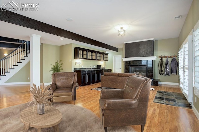 living room with sink, light hardwood / wood-style flooring, ornate columns, beam ceiling, and a tiled fireplace