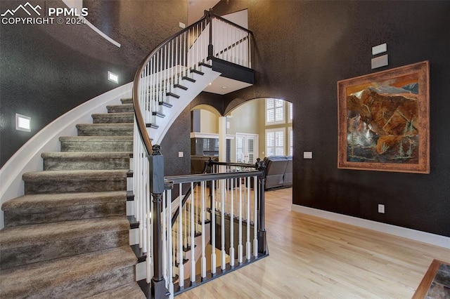 staircase with hardwood / wood-style floors, a textured ceiling, and high vaulted ceiling