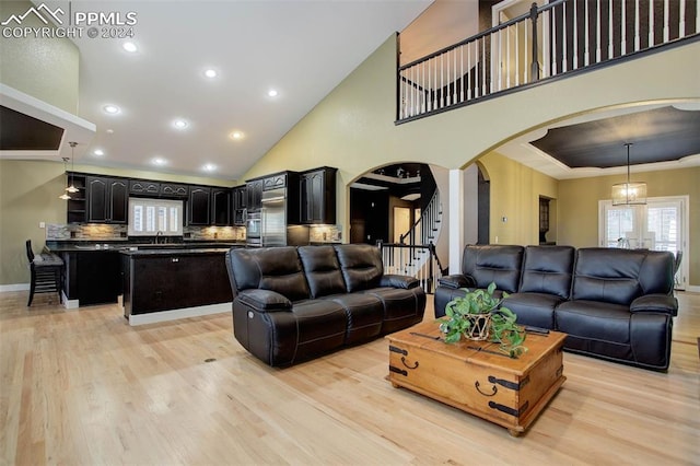 living room featuring sink, light hardwood / wood-style flooring, high vaulted ceiling, a notable chandelier, and crown molding