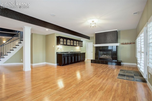 unfurnished living room with hardwood / wood-style flooring, beam ceiling, indoor wet bar, and a fireplace