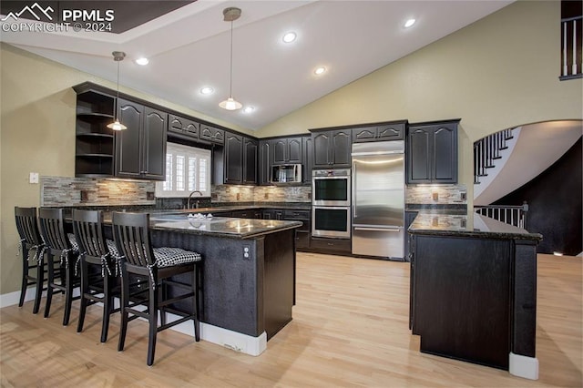 kitchen with kitchen peninsula, light wood-type flooring, tasteful backsplash, stainless steel appliances, and decorative light fixtures