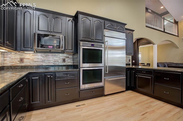 kitchen featuring decorative backsplash, light wood-type flooring, appliances with stainless steel finishes, and dark stone counters