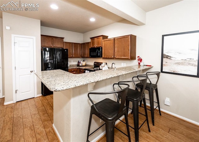 1441 Kempton Aly, Colorado Springs, CO 80910 - kitchen with black appliances, a peninsula, a kitchen bar, light wood-style floors, and recessed lighting