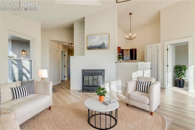 living room featuring a notable chandelier, a fireplace, high vaulted ceiling, and light hardwood / wood-style flooring