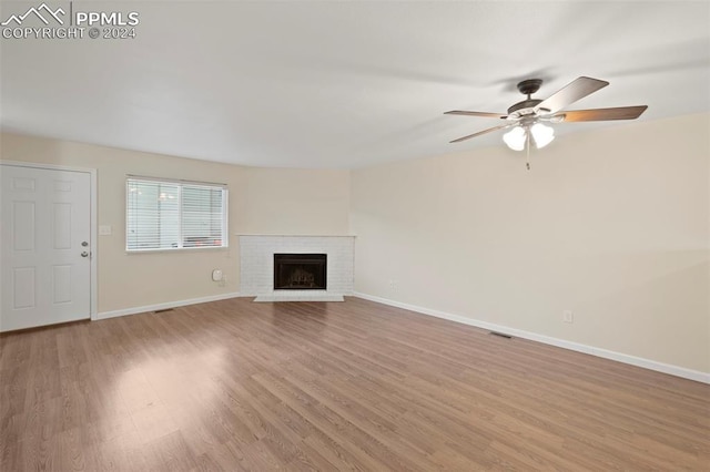 unfurnished living room with ceiling fan, light wood-type flooring, and a brick fireplace