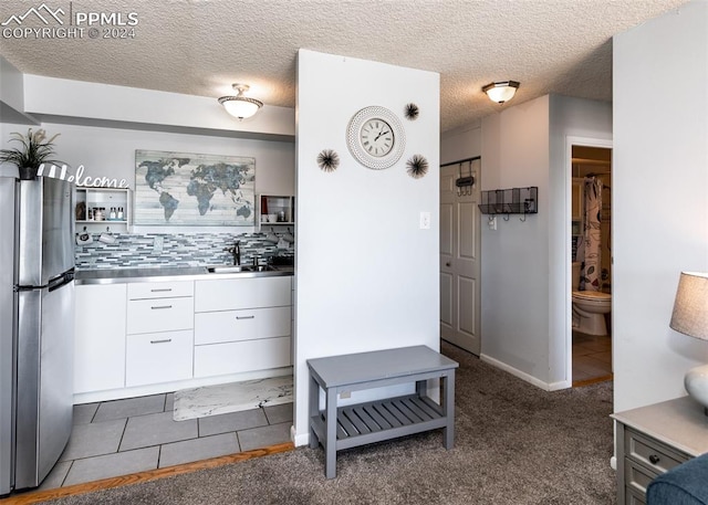 kitchen with decorative backsplash, dark carpet, white cabinetry, and stainless steel refrigerator