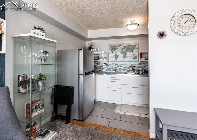 kitchen featuring stainless steel refrigerator, white cabinetry, stainless steel counters, dark tile patterned floors, and a textured ceiling