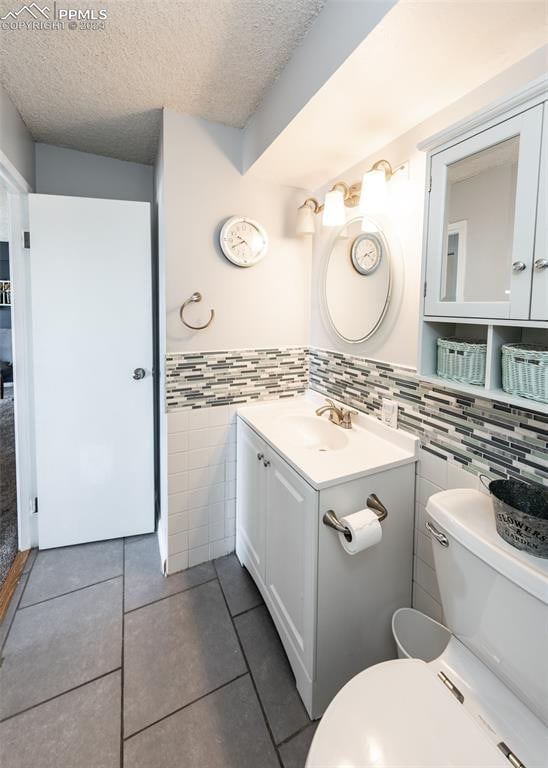 bathroom featuring vanity, tile patterned floors, toilet, tile walls, and a textured ceiling