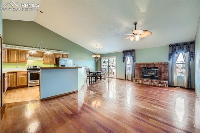 kitchen featuring a brick fireplace, light hardwood / wood-style flooring, pendant lighting, ceiling fan with notable chandelier, and appliances with stainless steel finishes