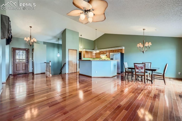 kitchen featuring ceiling fan with notable chandelier, kitchen peninsula, vaulted ceiling, wood-type flooring, and stainless steel refrigerator