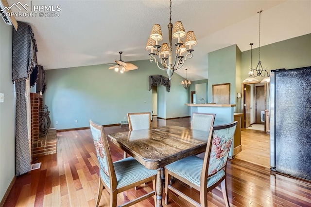 dining space featuring hardwood / wood-style flooring, ceiling fan with notable chandelier, and vaulted ceiling