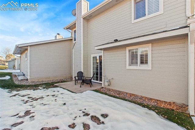 snow covered back of property featuring a patio area