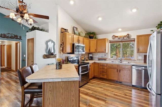 kitchen featuring kitchen peninsula, appliances with stainless steel finishes, a kitchen breakfast bar, sink, and light hardwood / wood-style floors