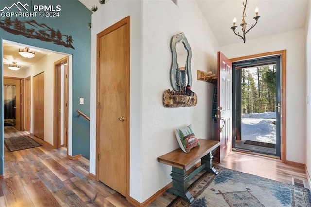 foyer entrance featuring wood-type flooring, vaulted ceiling, and an inviting chandelier