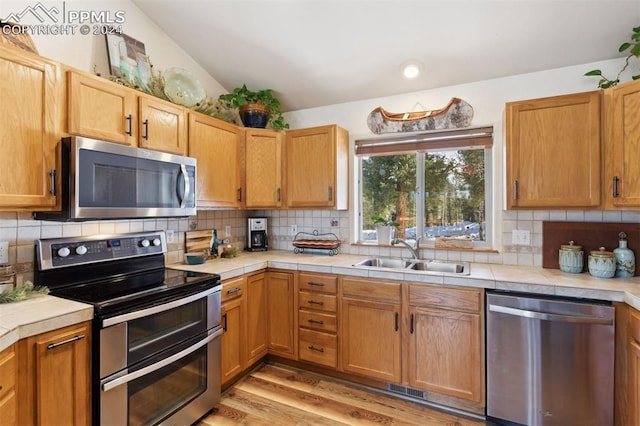 kitchen featuring sink, stainless steel appliances, backsplash, light hardwood / wood-style floors, and lofted ceiling