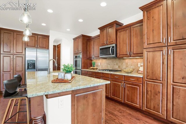 2933 Cathedral Park Vw, Colorado Springs, CO 80904 - kitchen featuring appliances with stainless steel finishes, arched walkways, light stone counters, a sink, and a breakfast bar area