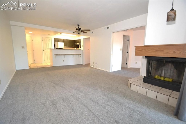 unfurnished living room featuring carpet flooring, a tiled fireplace, and ceiling fan