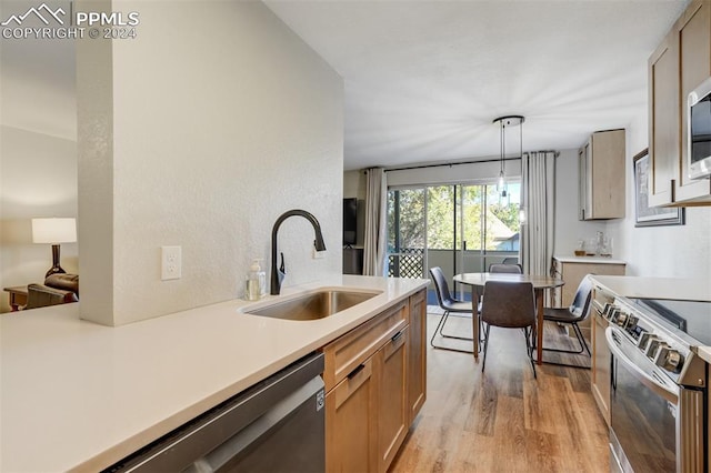 kitchen with stainless steel appliances, light hardwood / wood-style flooring, hanging light fixtures, and sink