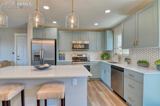 kitchen featuring hanging light fixtures, sink, light wood-type flooring, appliances with stainless steel finishes, and a kitchen bar