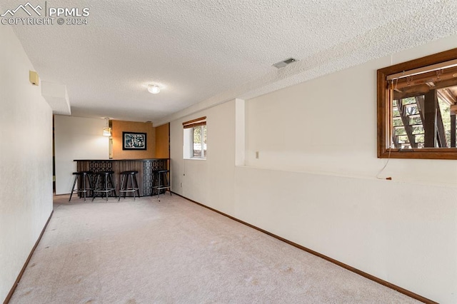 basement featuring a textured ceiling, a wealth of natural light, carpet, and indoor bar