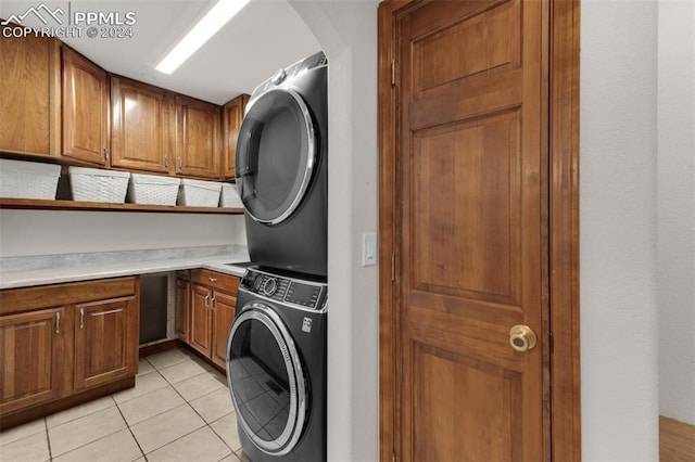 clothes washing area with light tile patterned flooring, cabinets, and stacked washing maching and dryer