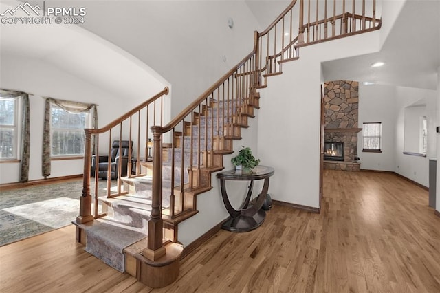 staircase featuring a stone fireplace, wood-type flooring, and high vaulted ceiling