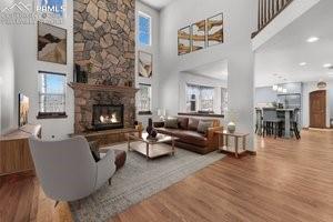 living room with a stone fireplace, wood-type flooring, and a high ceiling