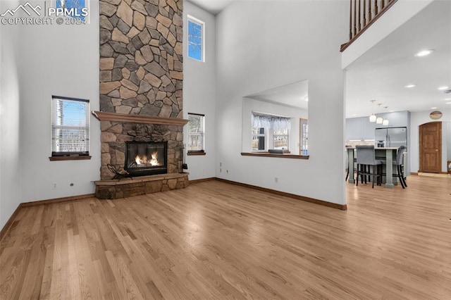 unfurnished living room with a fireplace, light hardwood / wood-style flooring, a towering ceiling, and a healthy amount of sunlight