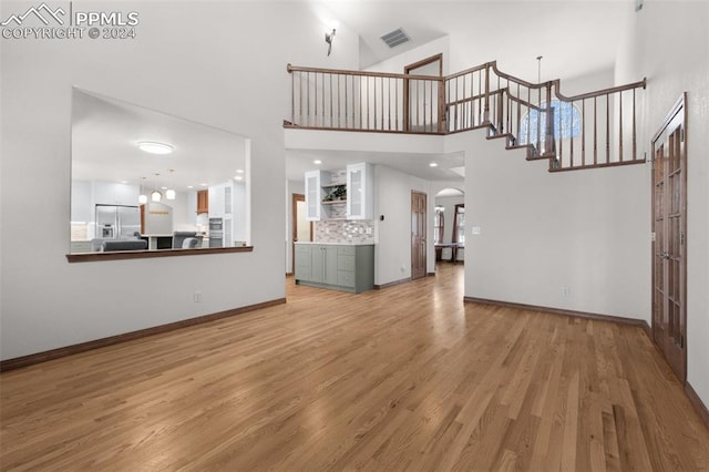 unfurnished living room featuring a towering ceiling and light wood-type flooring