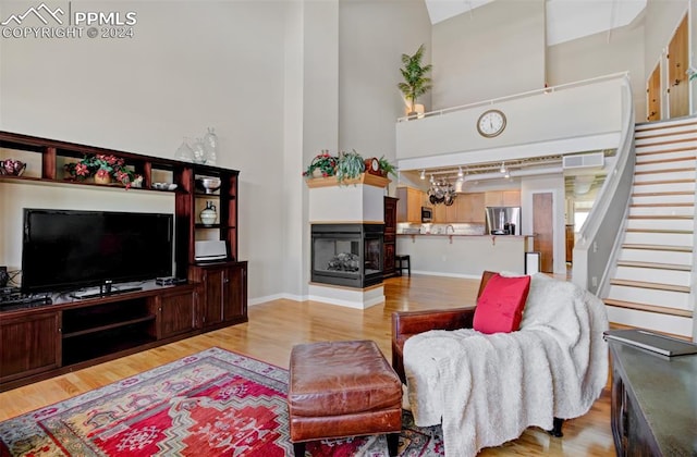 living room featuring a multi sided fireplace, a towering ceiling, track lighting, and light hardwood / wood-style flooring