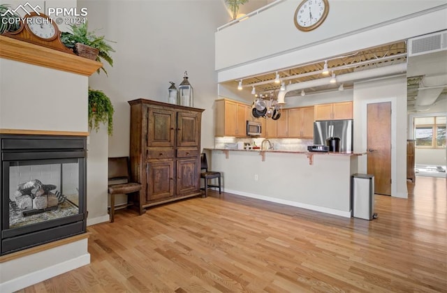 kitchen featuring rail lighting, stainless steel appliances, kitchen peninsula, light hardwood / wood-style floors, and decorative backsplash