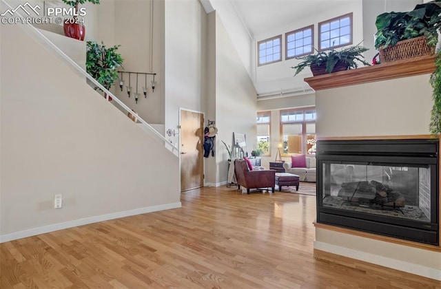 foyer entrance with light wood-type flooring, a towering ceiling, and a multi sided fireplace